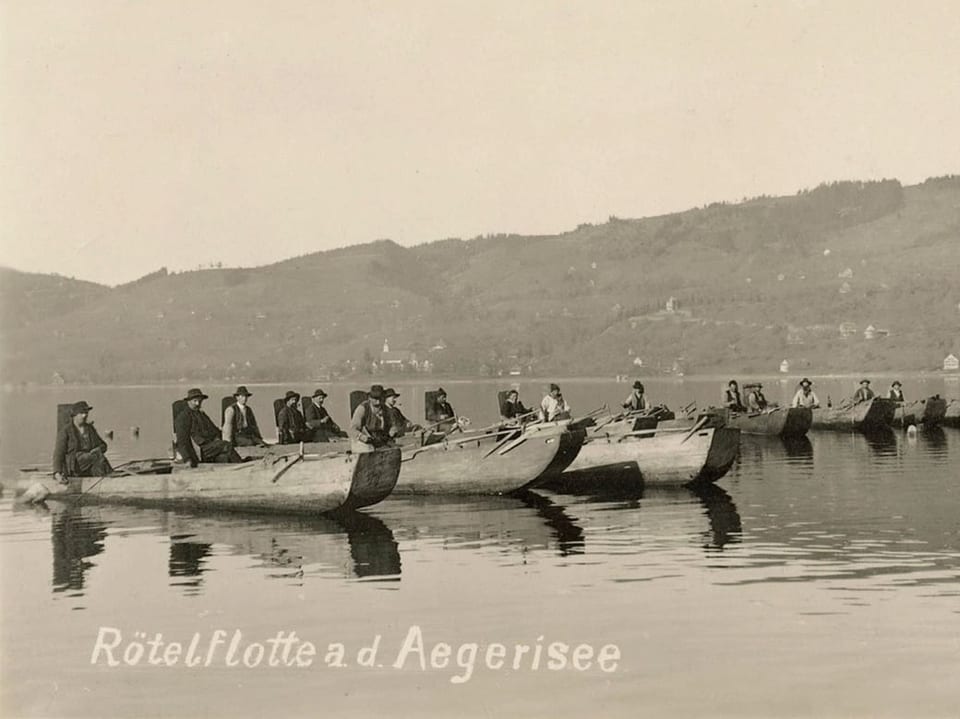 Die Schwarz-Weiss-Fotografie zeigt Fischer in Holzbooten auf dem Ägerisee.