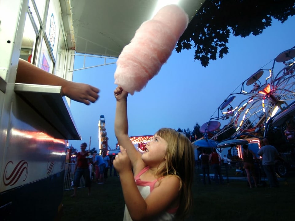 Ein Mädchen kauft eine rosa Zuckerwatte am Jahrmarkt.
