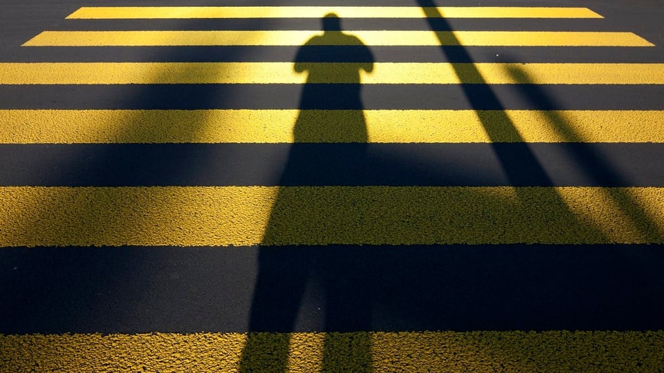 Schatten eines Menschen auf einem Fussgängerstreifen.