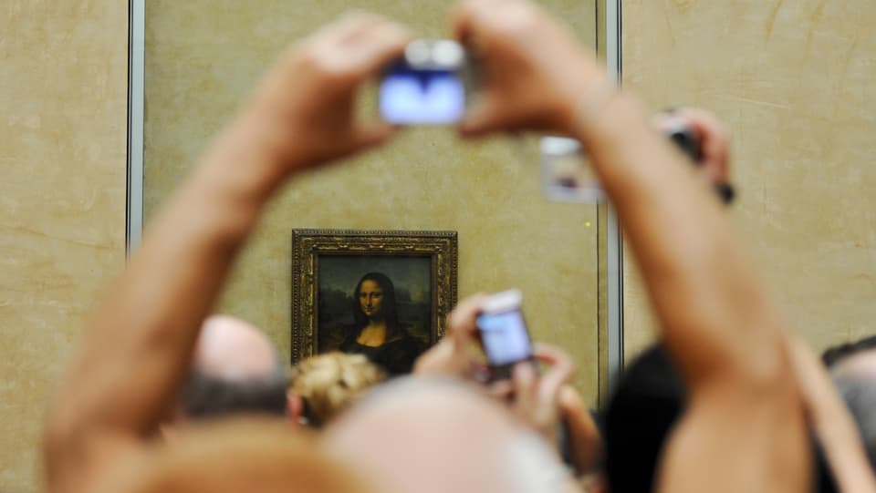 Hände mit Fotokameras in der Hand vor dem Bild der Mona Lisa.