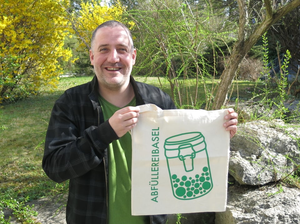 Mann zeigt eine Stofftasche mit der Aufschrift «Abfüllerei Basel».