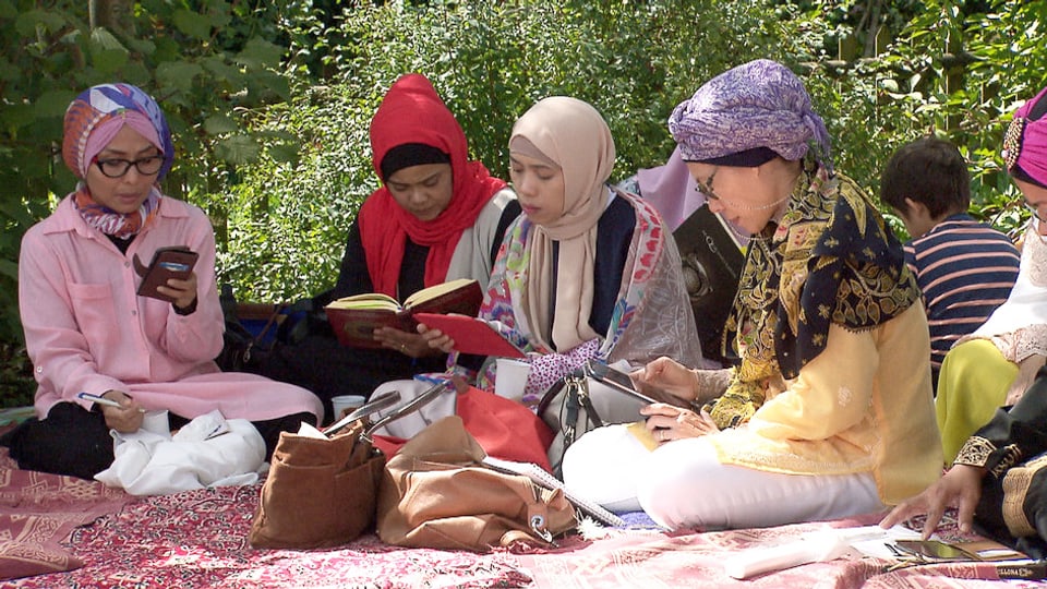 Muslimische Frauen sitzen in einem Garten auf bunten Tüchern