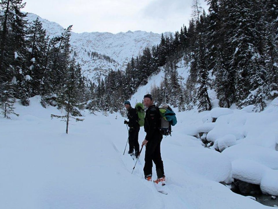 Zwei Männer mit Ski und Rucksack im verschneiten Wald