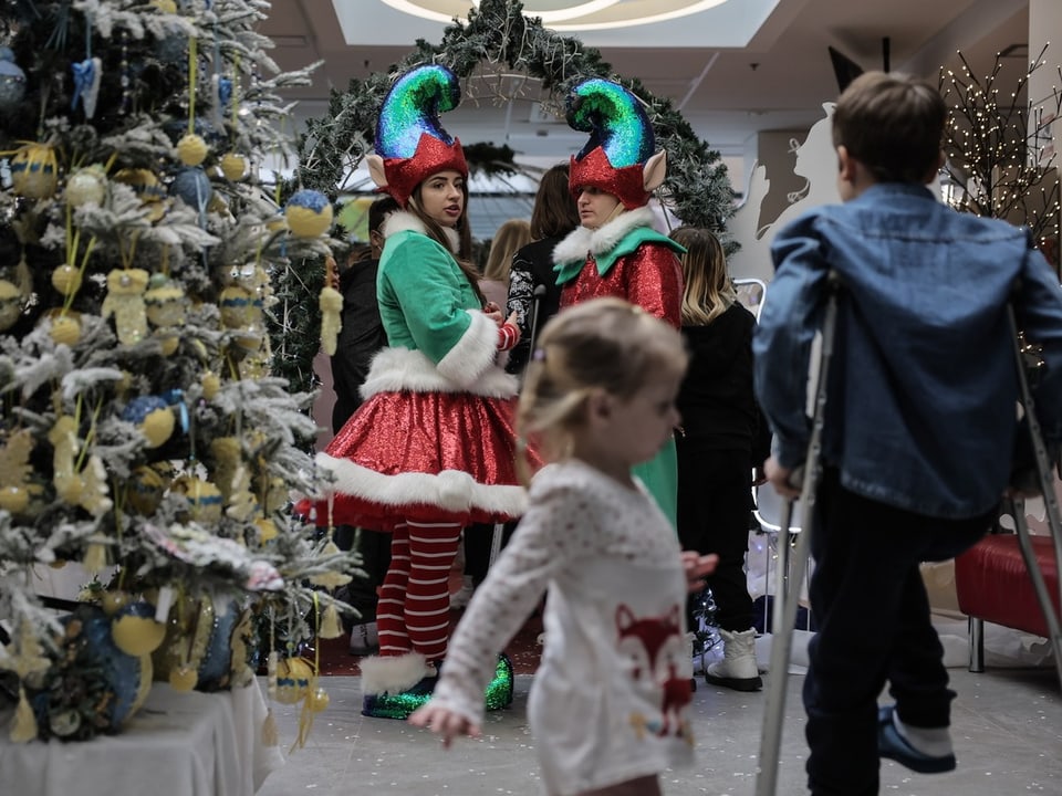 Zwei verkleidete Personen in Elfenkostümen sind umgeben von Kindern im weihnachtlich dekorierten Spital.