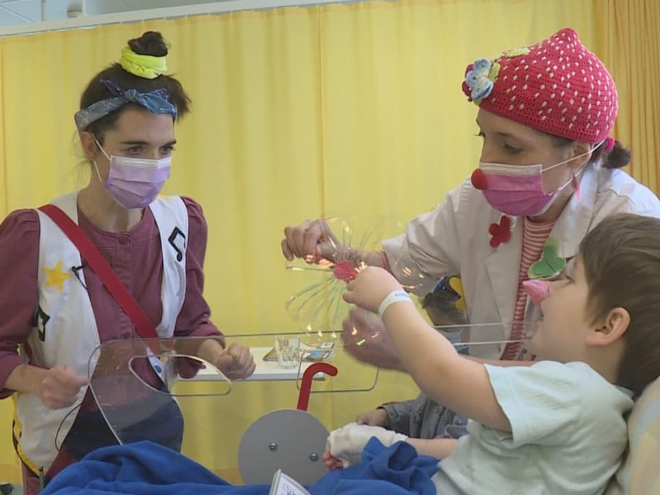 Zwei Clowns zeigen einem Jungen im Krankenbett einen Zaubertrick.