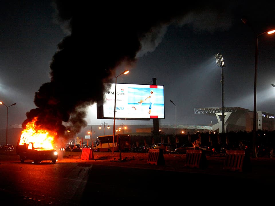 Im Vordergund steht brennendes Auto. Im Hintergrund ist das Stadion zu sehen