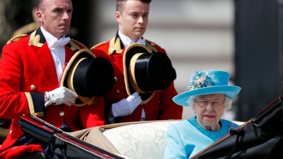 Die Queen sitzend mit blauem Hut in einer Kutsche. 