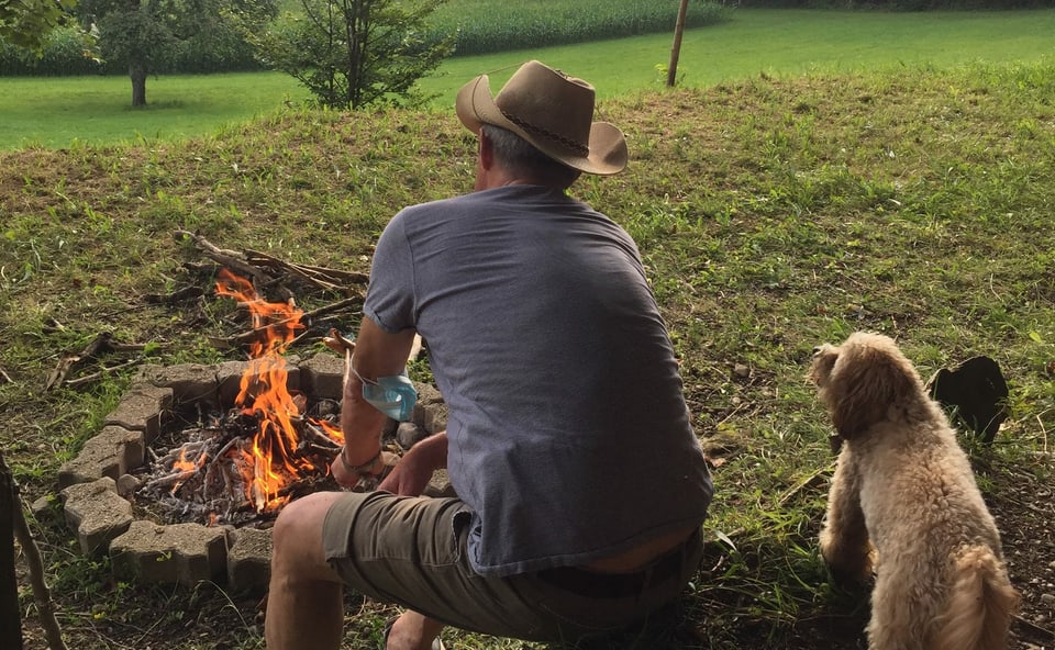 Mann sitzt mit Hund am Feuer