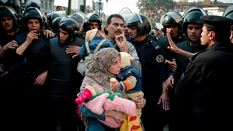 Ein Man und eine Frau mit Kind zwischen Polizisten mit Helmen.