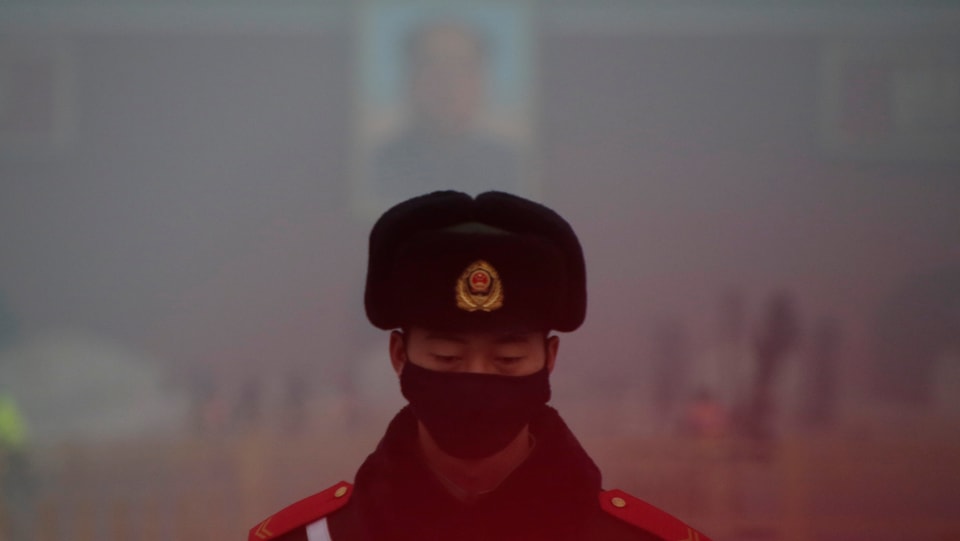 Chinesischer Beamte mit Maske vor Mao-Plakat im Dunst
