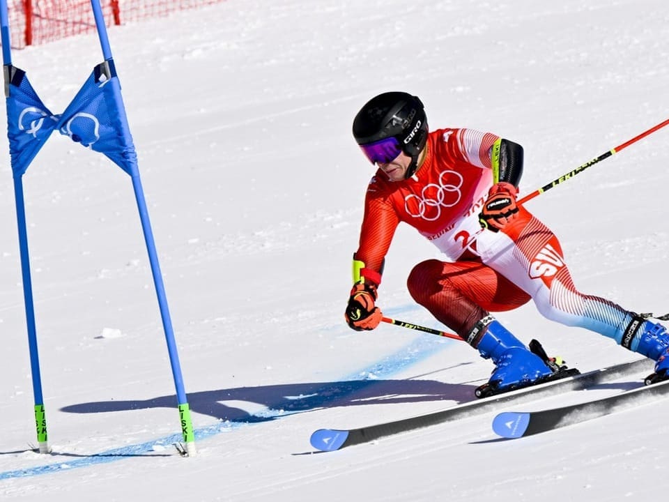 Ein Skifahrer mit Schweizer Anzug fährt an einem Fähnchen vorbei.
