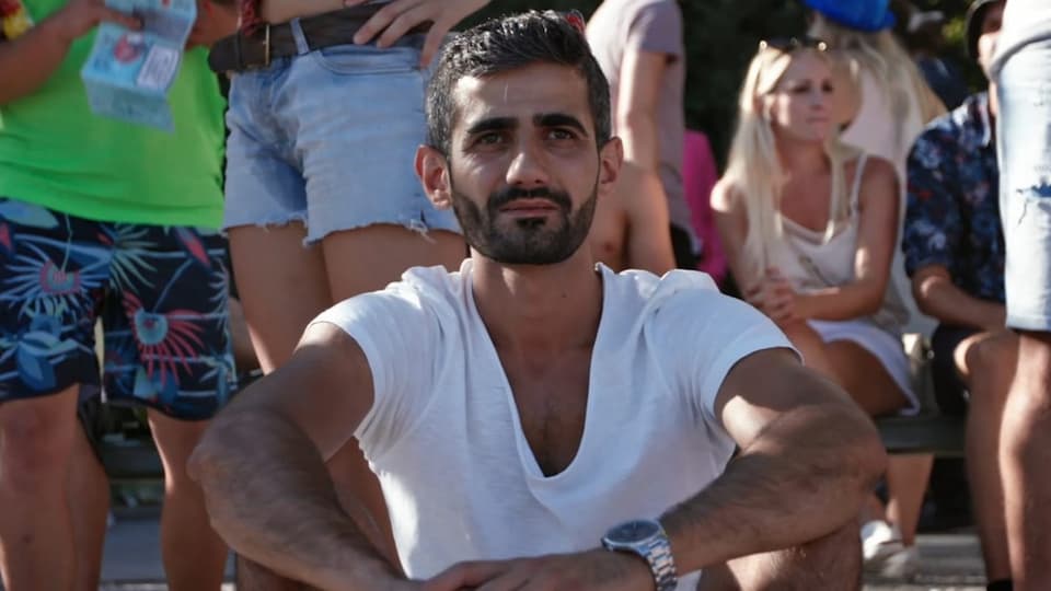 Amir, ein Geflüchteter aus der Türkei, nachdenklich inmitten sommerlich gekleideter Menschen.