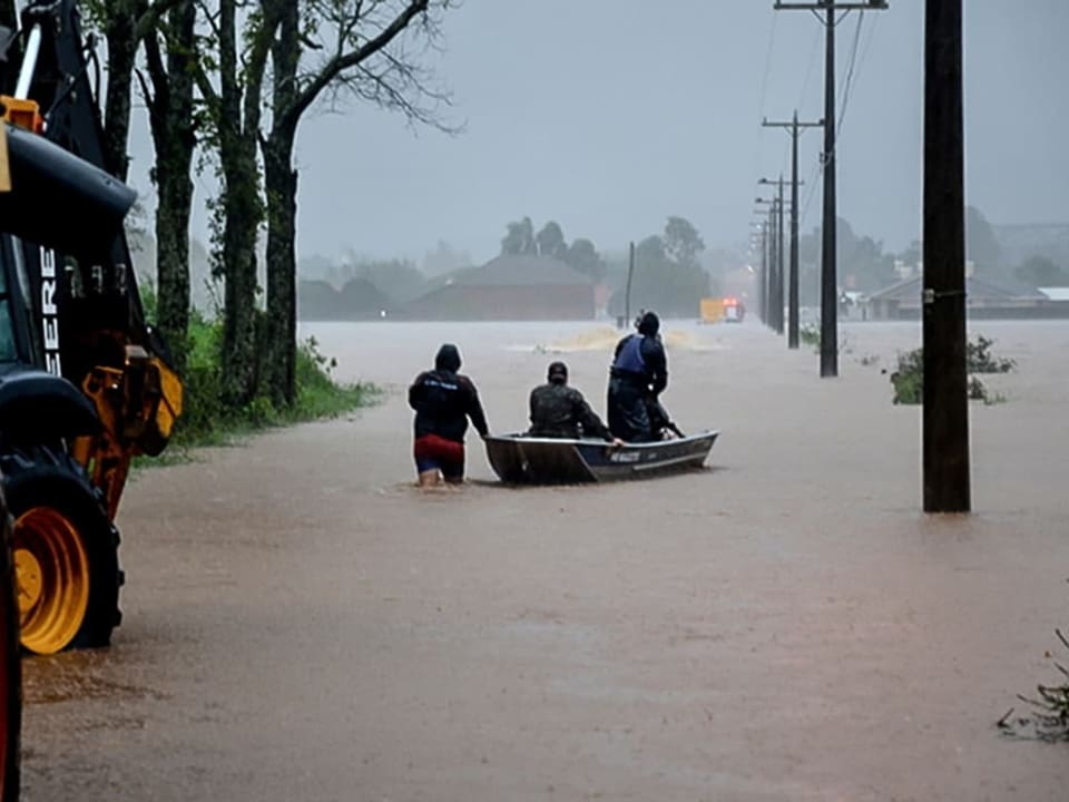 Menschen sitzen in einem Boot auf einer überfluteten Strasse.