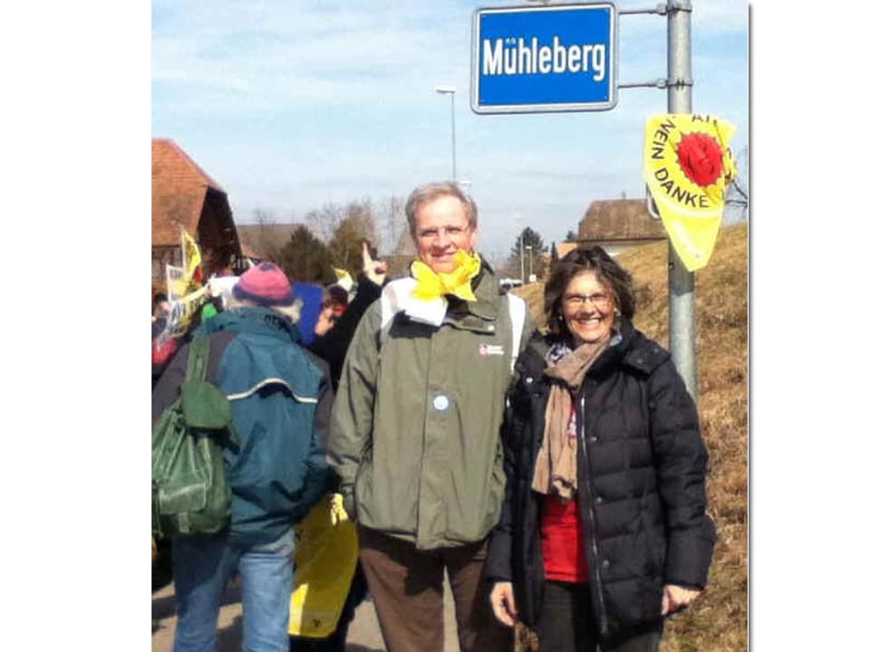 Eine Frau und ein mann posieren vor dem Ortsschild Mühleberg.