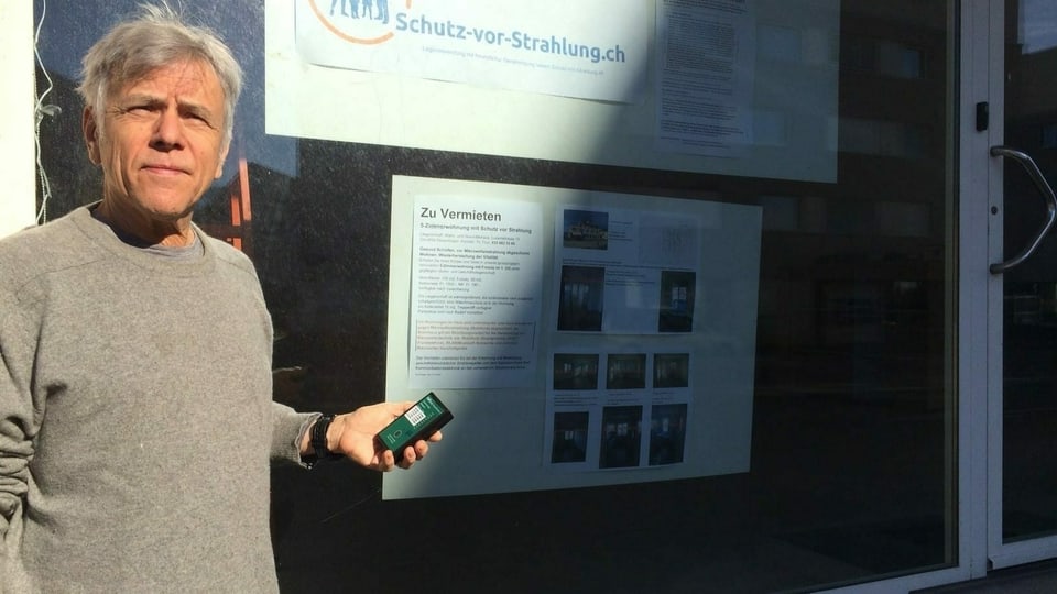 Mann in grauem Pullover hält Handy in Hand.