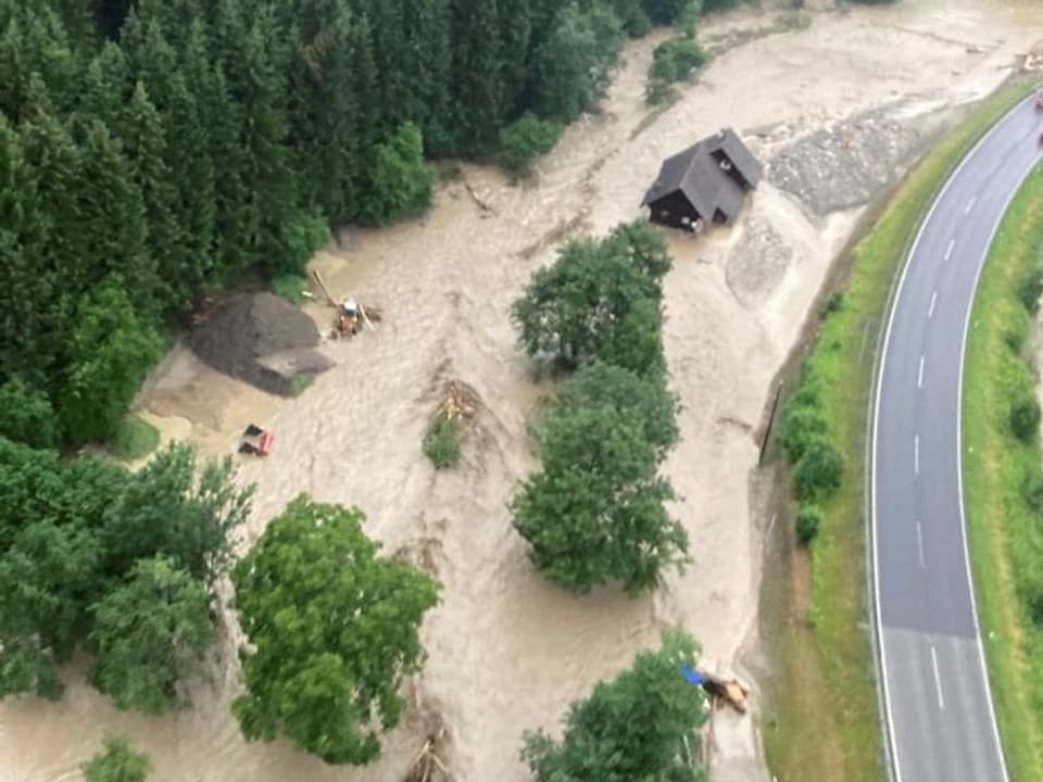 Ein Fluss ist über die Ufer getreten. Dabei stehen mehrere Häuser im neben einer Strasse unter ca. 1 Meter hohem Wasser.