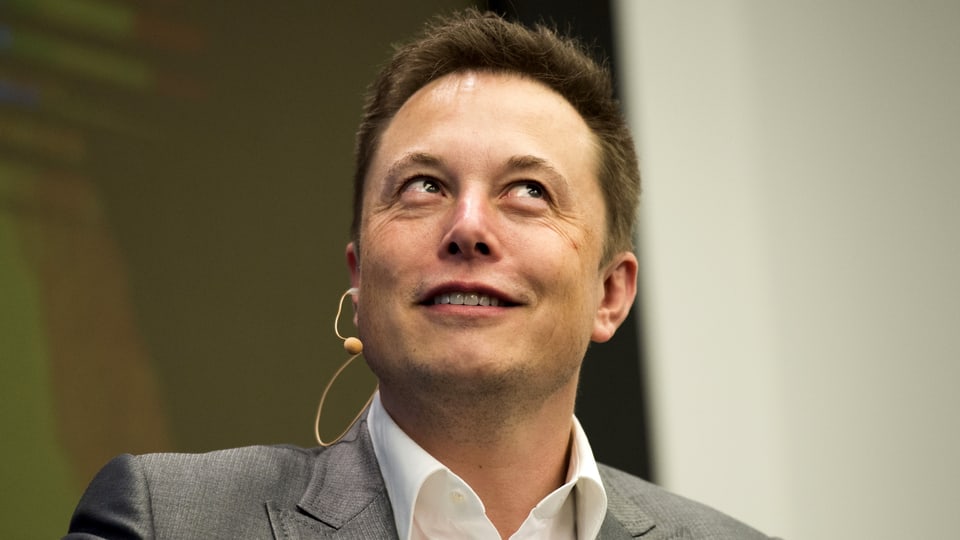 Elon Musk mit einem Mikro am Ohr, schaut nach oben.