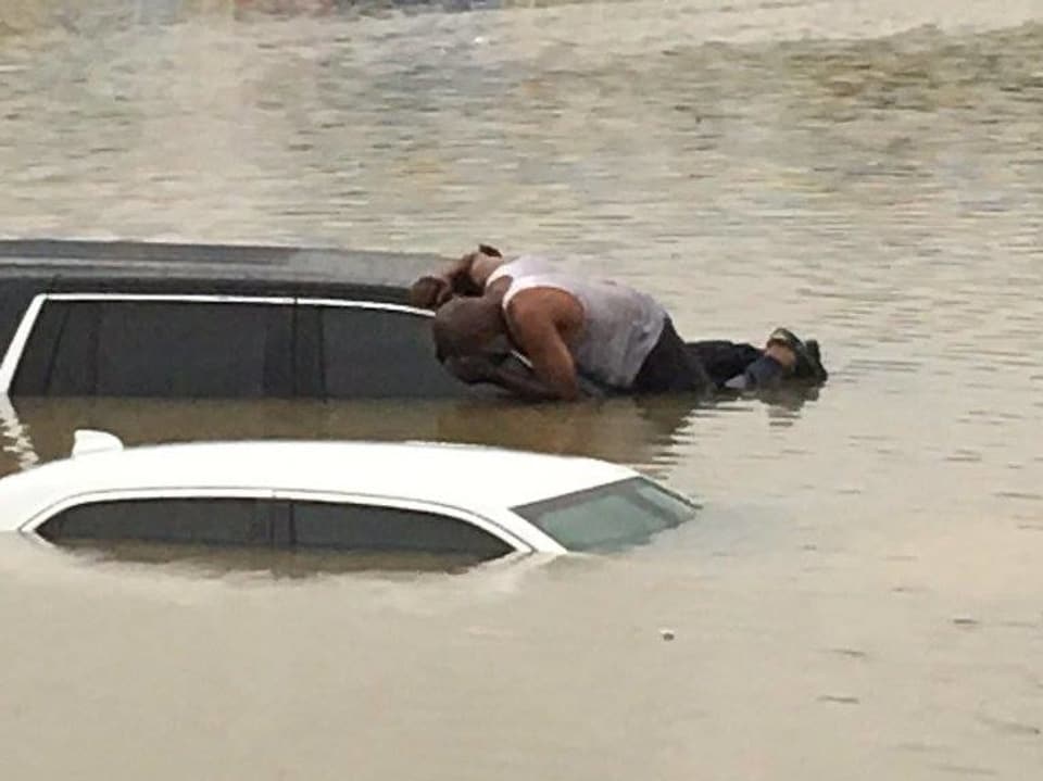 Ein Mann versucht in ein Auto zu schauen. Dies steht fast bis zum Dach im Wasser.