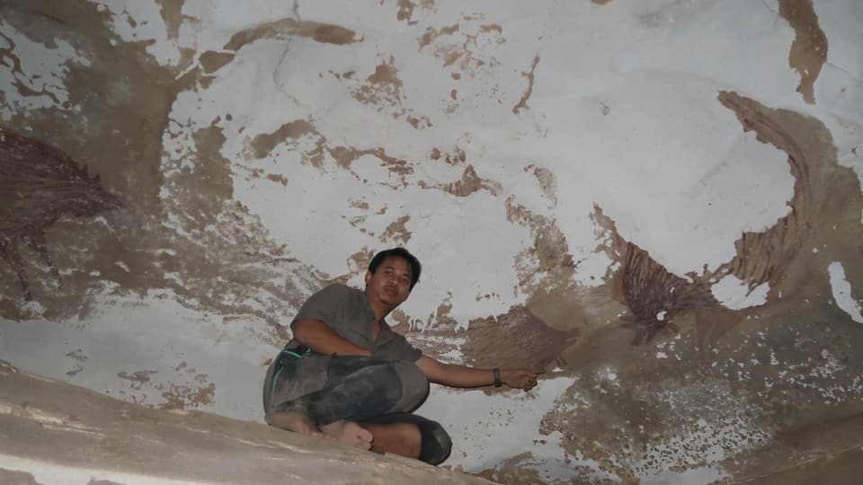 Mann kniet in einer Höhle neben einer Malerei