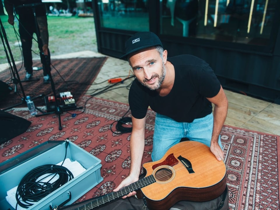 Ein Mann kniet am Boden, vor ihm seine Akustikgitarre.