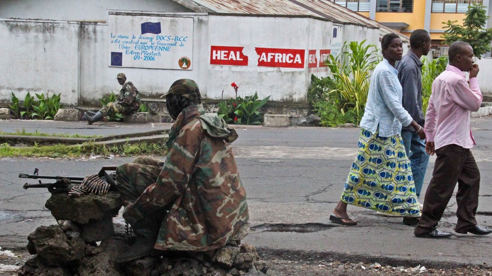 Rebellen überwachen eine Strasse im Zentrum Gomas, während Zivilisten über die Strasse laufen.