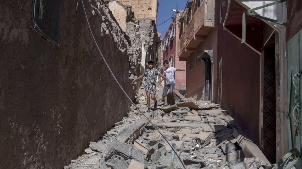 Zwei Buben gehen eine Strasse voller Trümmer in Marrakesch entlang.
