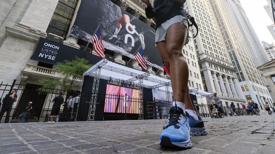 Eine Frau mit On-Sportschuhen vor der New York Stock Exchange an der Wall Street in New York