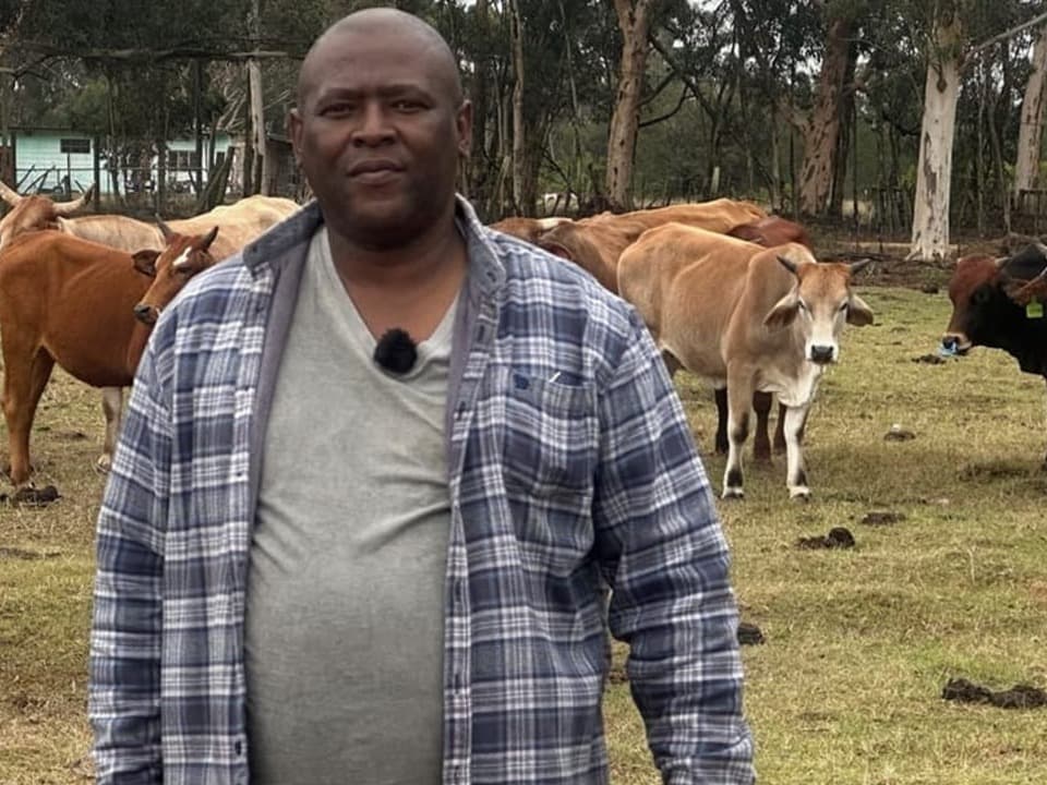 Das Bild zeigt Lindile Ndimba, der vor seinen Kühen posiert.