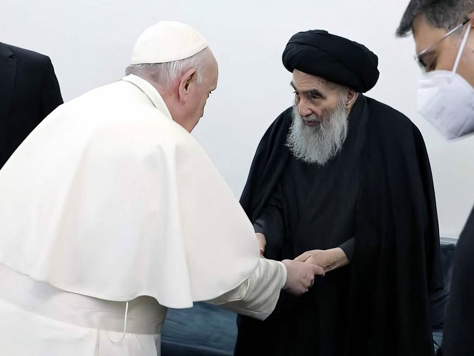 Papst Franziskus (in weissem Gewand) schüttelt die Hände von Ayatollah Ali al-Sistani (in schwarz gehüllt)