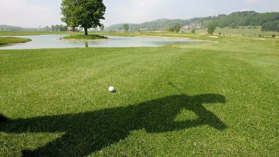 Ein Schatten eines Golfers, ein Golfball auf dem Rasen.
