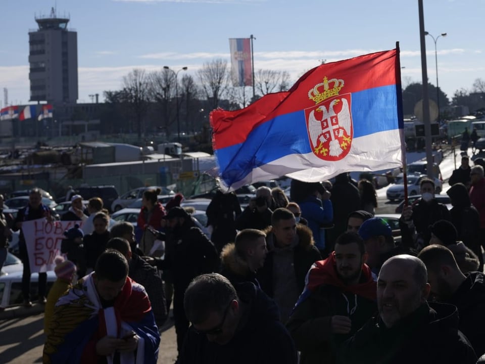 Fans von Djokovic warten am Terminal mit einer serbischen Flagge.