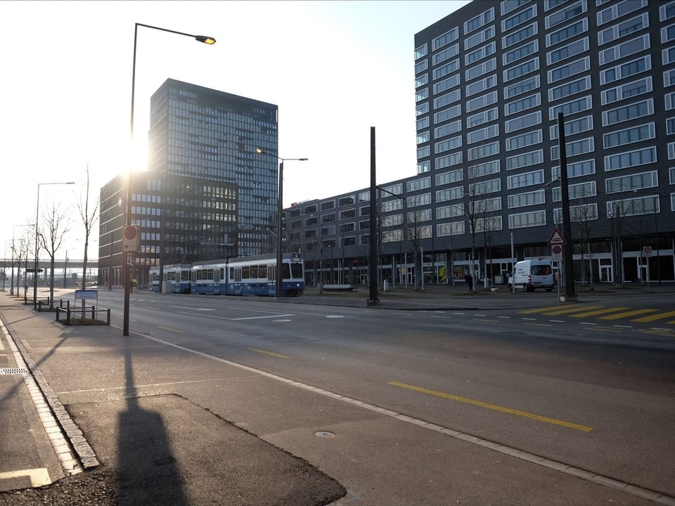 Ein Tram fährt in der Morgensonne vor moderner Gebäudekulisse.