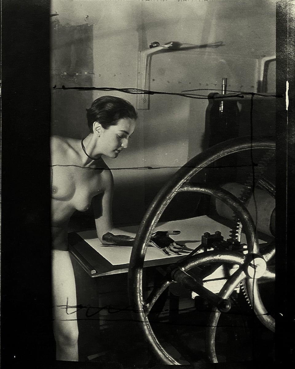 Schwarz-Weiss-Foto mit nackter Meret Oppenheim an einer Druckerpresse. Ihre Hand ist mit Druckerschwärze angemalt.