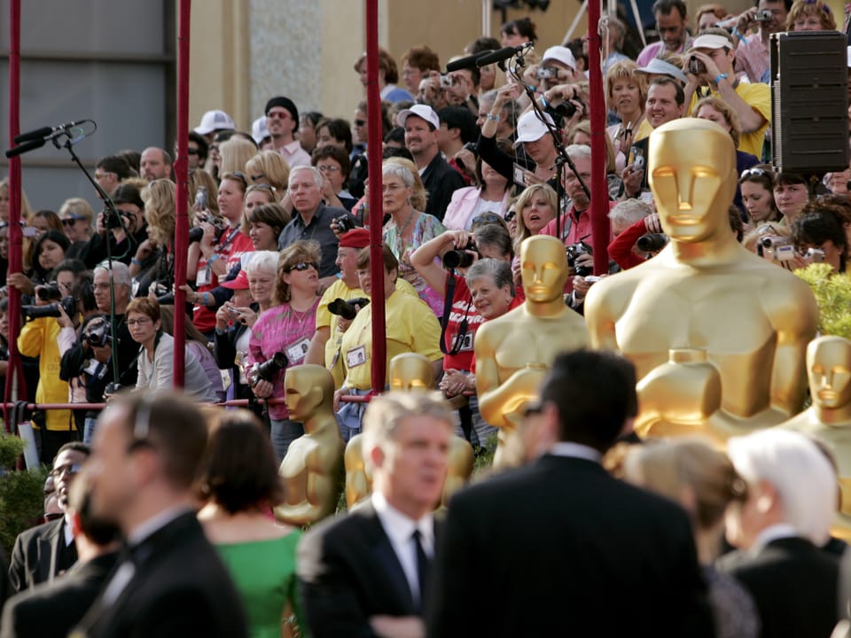 Menschenmenge auf einer Tribühne sitzen. Vor ihnen stehen übergrosse Oscar-Figuren.