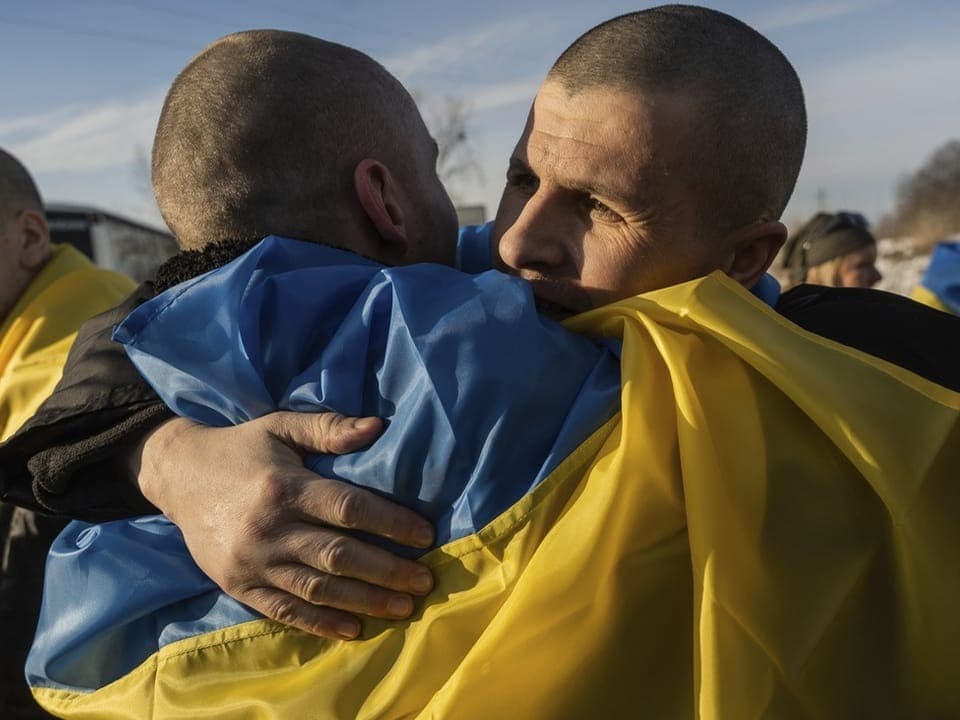zwei Ukrainische Soldaten umarmen sich, umhüllt in der ukrainischen Flagge.