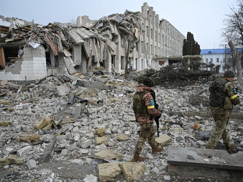 Ukrainische Militärangehörige gehen in der Nähe eines durch Beschuss zerstörten Schulgebäudes.