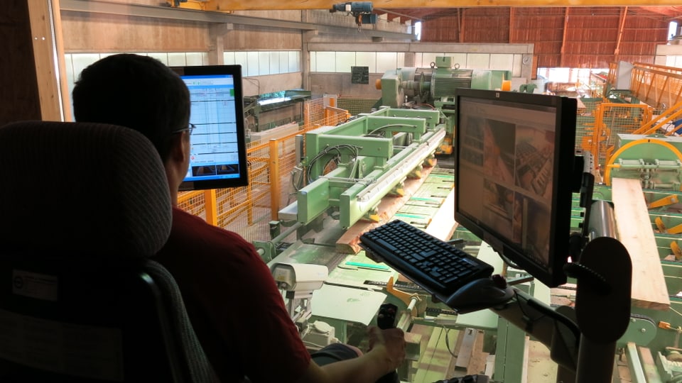 Ein Man sitzt in einem Kontrollzentrum in einer Sägerei und bedient Maschinen 
