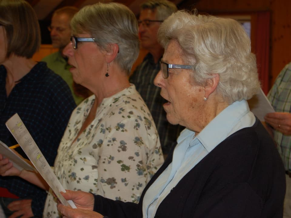 Zwei ältere Frauen mit Notenblättern beim Singen.