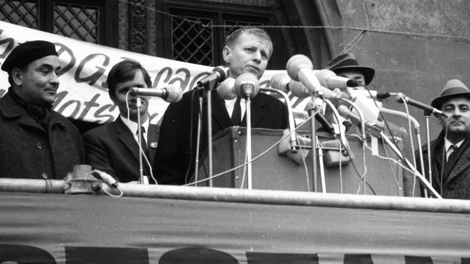 ein schwarz-weiss Foto eines jüngeren Mannes am Rednerpult