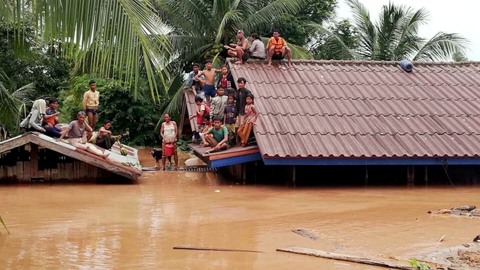 Menschen stehen und sitzen auf Dächern, ihre Häuser stehen unter Wasser
