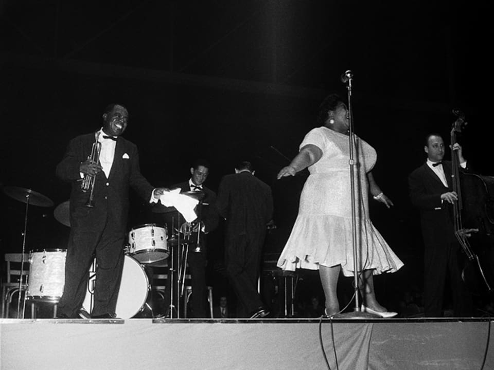 Louis Armstrong auf der Bühne im Hallenstadion. Mit dabei eine Frau in einem weissen Kleid.