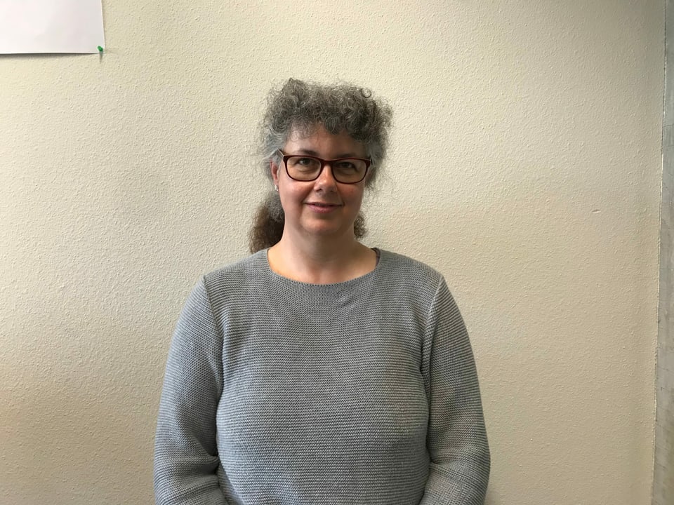 Im Bild ist Claudia Spiess von der Uni Zürich. Sie leitet das Forschungsprojekt Disabeld in Politics. Sie ist eine ältere Frau mit grauen langen Haaren und Brille im grauen Pullover.