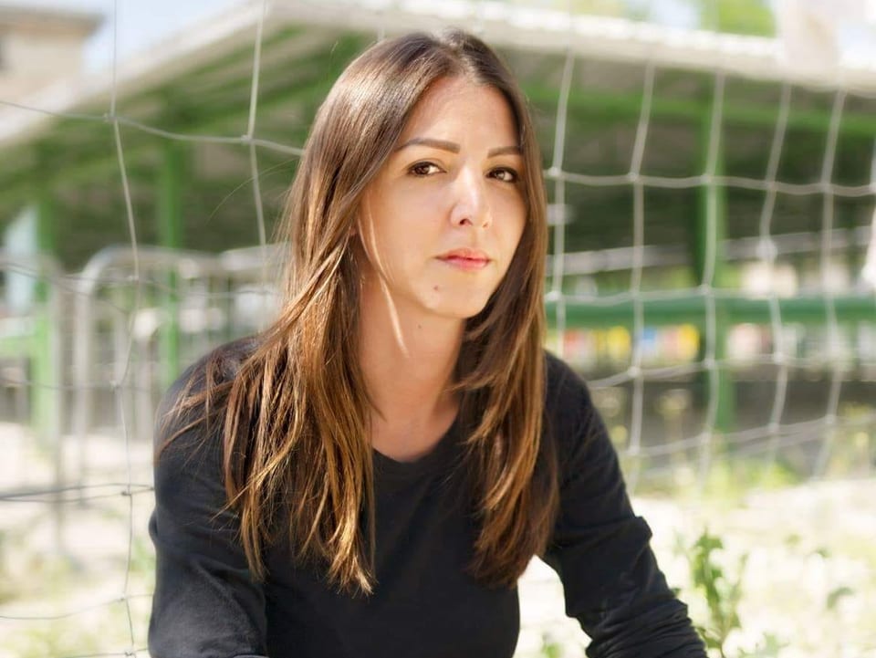 Ein Porträtfoto von Vanja Crnojevic, einer jungen Frau, mit braunen Haaren und schwarzem Pullover. Sie sitzt vor einem Zaun und blickt enschlossen in die Kamera.
