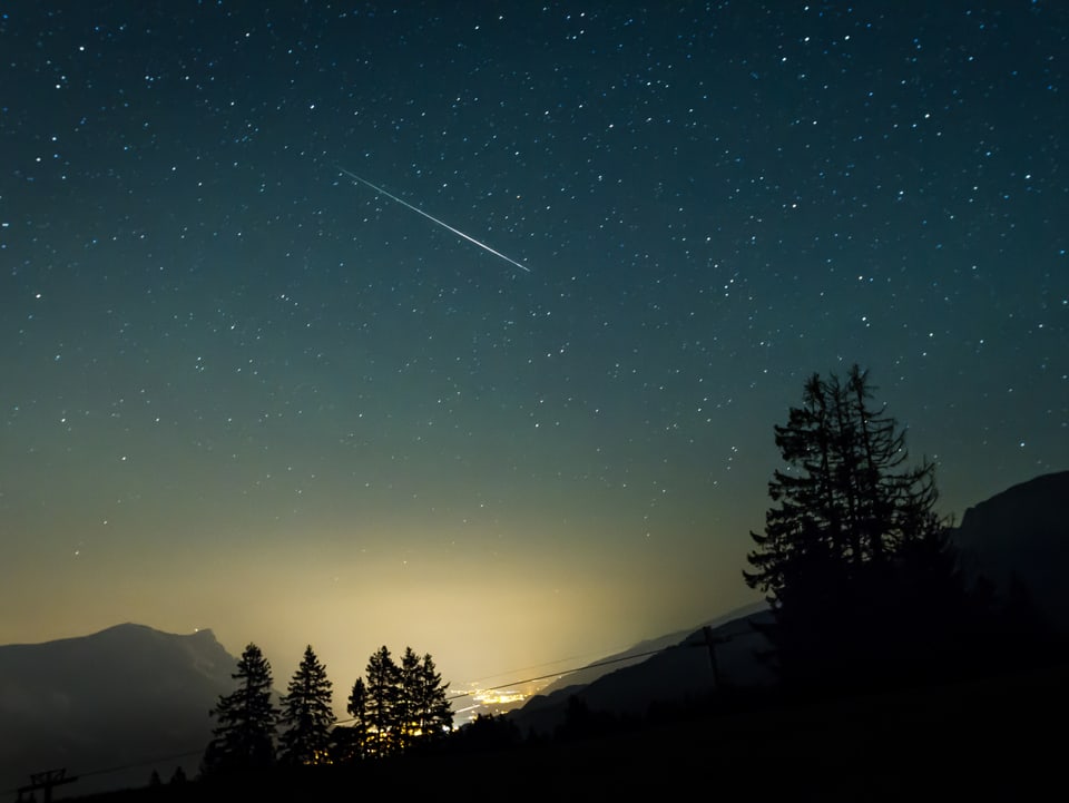 Das Lichtermeer des Sarganserlands erhellt den unteren Teil des Himmel. Darüber ein Sternenhimmel mit einer einzigen Sternschnuppe.