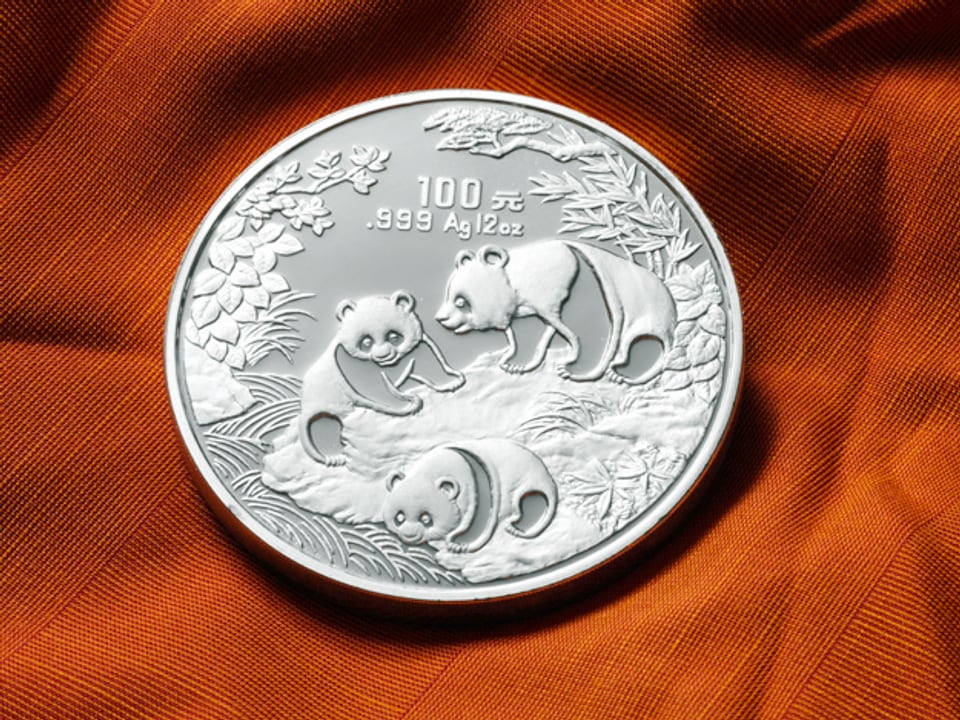 Eine silberne Münze mit drei Pandabären als Motiv und chinesischen Schriftzeichen.
