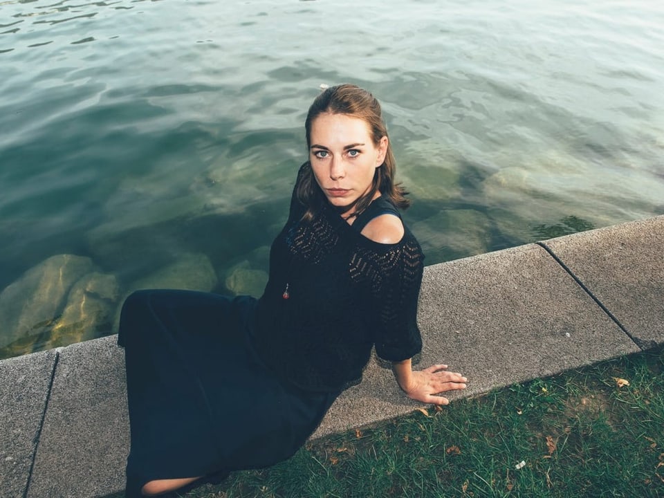 Eine Frau sitzt im schwarzen Kleid am Wasser