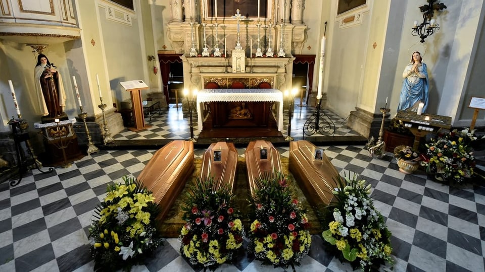 Vier Holzsärge sind vor einem Altar einer Kirche.