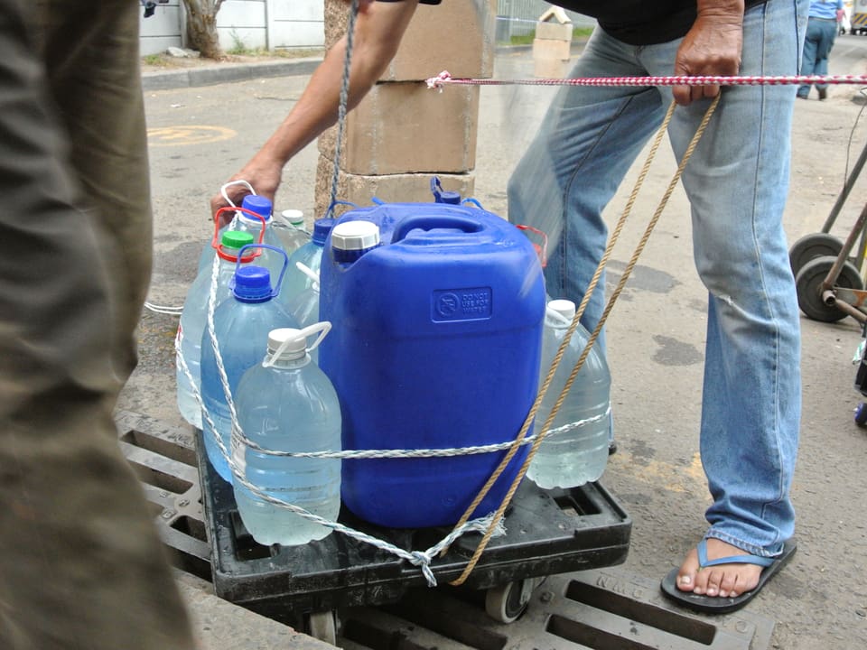 Ein Mann packt Wasserkanister auf ein Wägelchen.