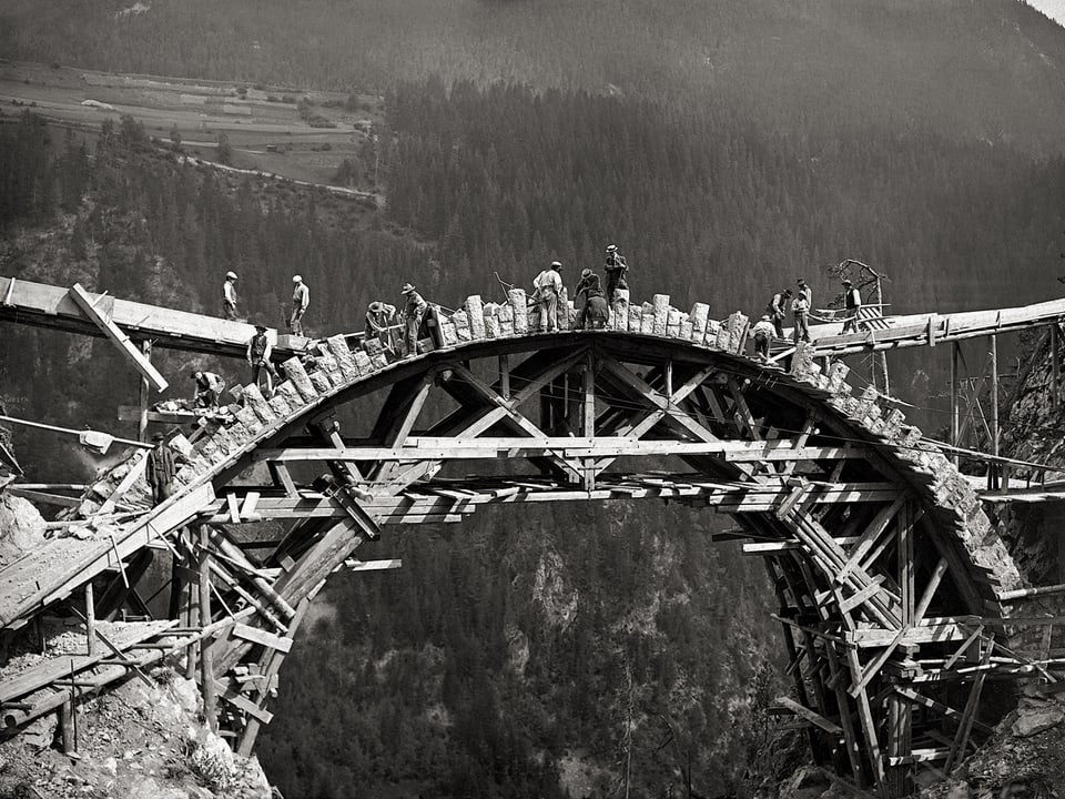Auf dem Lehrgerüst des Pflanzgartenviadukt im Jahr 1908 sieht man Arbeiter, die an den ersten Lagen grosser Steine schaffen.
