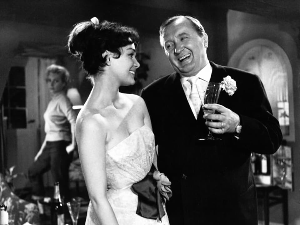 Ein Schauspieler und eine Frau im Abendkleid in einer Bar.